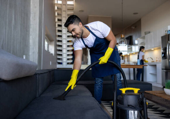 clean Professional Latin American cleaner vacuuming a sofa at an apartment - housework concepts